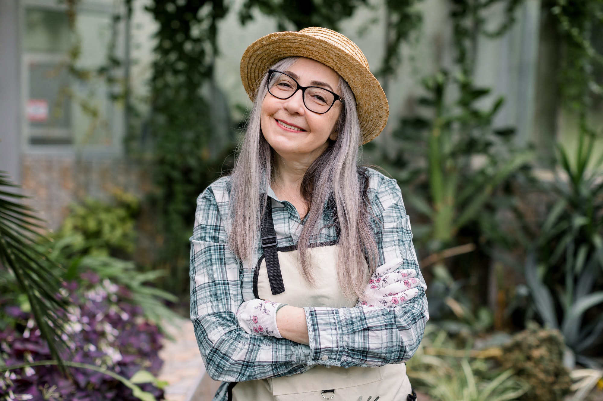 Close up of happy smiling senior lady gardener with long grey hair, wearing straw hat