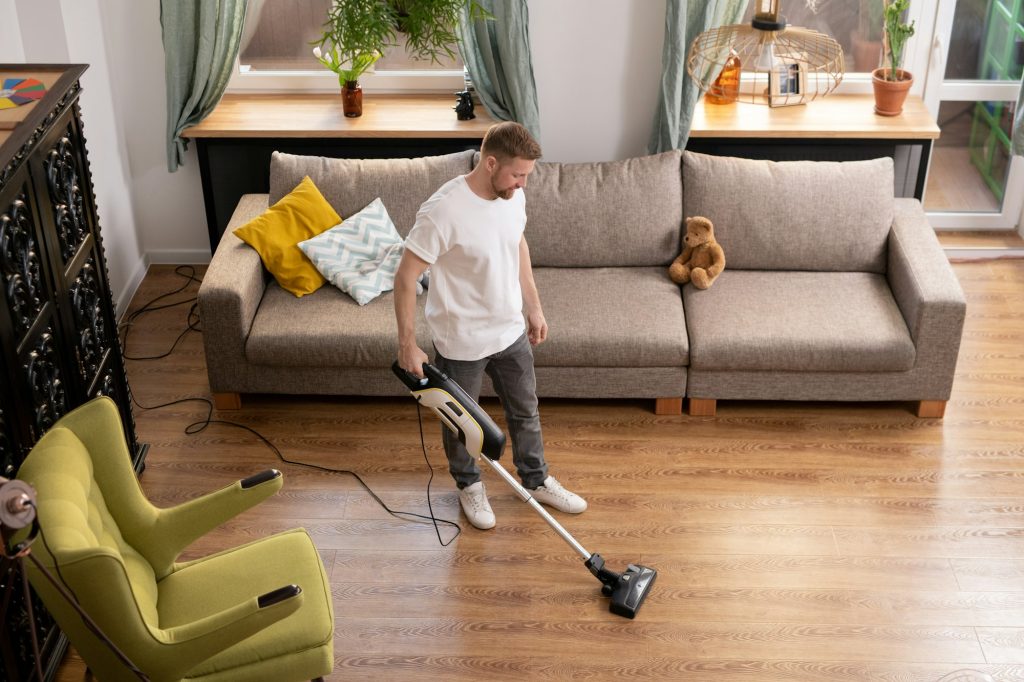 Young man doing domestic work while cleaning floor with vacuum cleaner